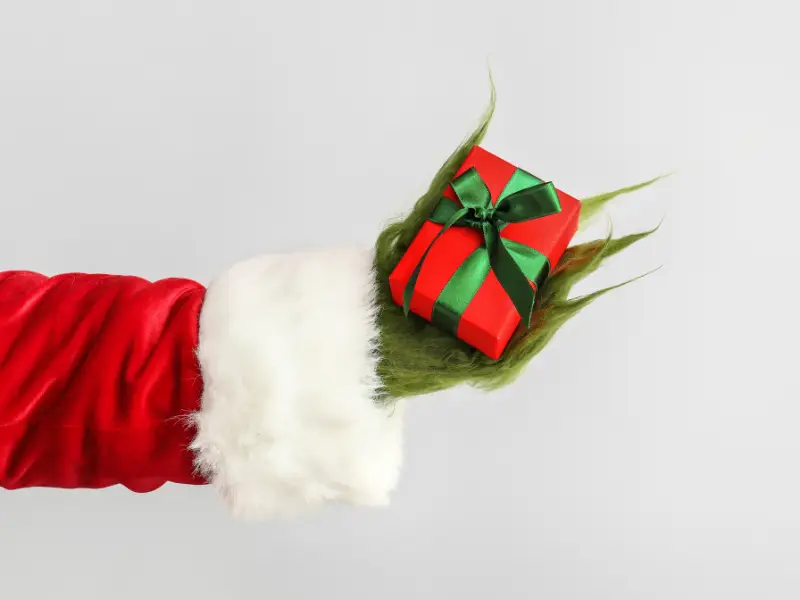 The Grinch's hand, dressed like Santa holding a red present with a green bow.